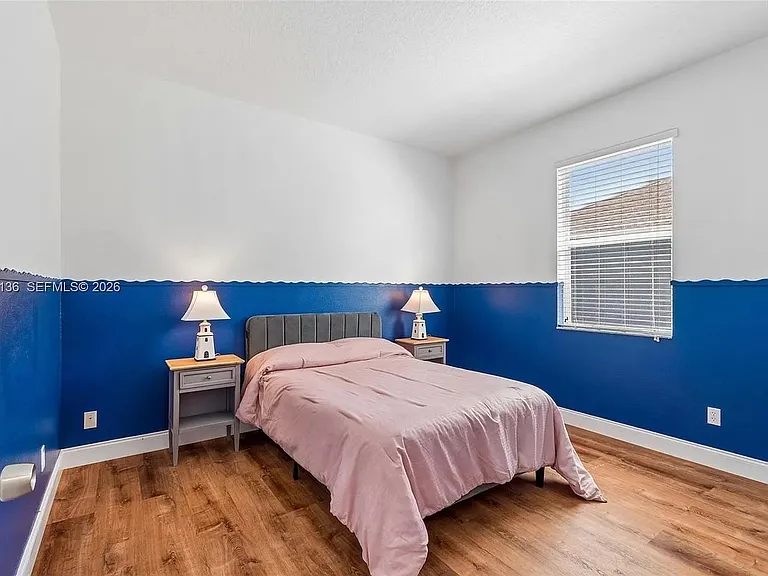 Furnished bedroom with wood-look flooring, a full bed with nightstands, and a window with blinds for natural light.