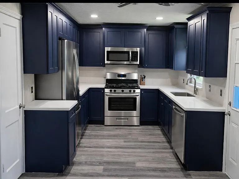 Updated U-shaped kitchen with navy cabinetry, quartz-style counters, and stainless steel range, microwave, fridge, and dishwa