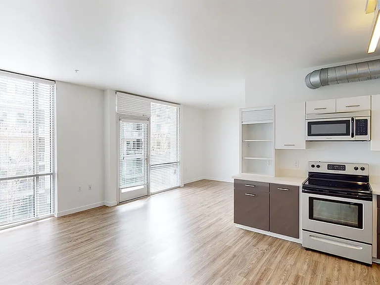Apartment kitchen with stainless steel appliances, dining and living room with wood-style flooring.