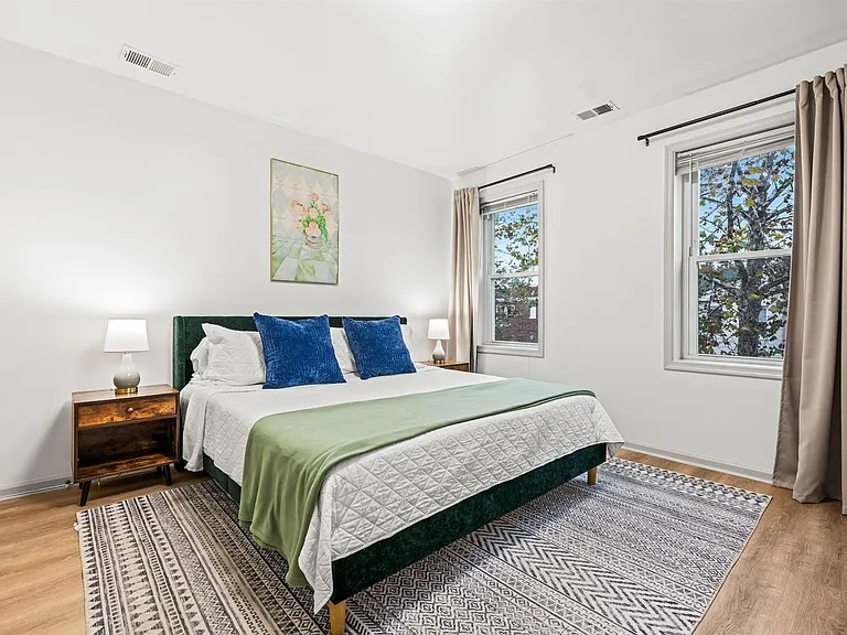 Spacious bedroom with a queen bed, side tables, and large windows with curtains for privacy and natural light.