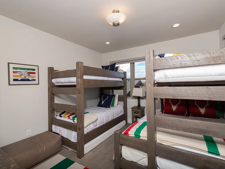 Upper-level bunk bedroom featuring a queen bed and three twin beds_comfortably sleeping up to five guests in a cozy, mountain-inspired setting.