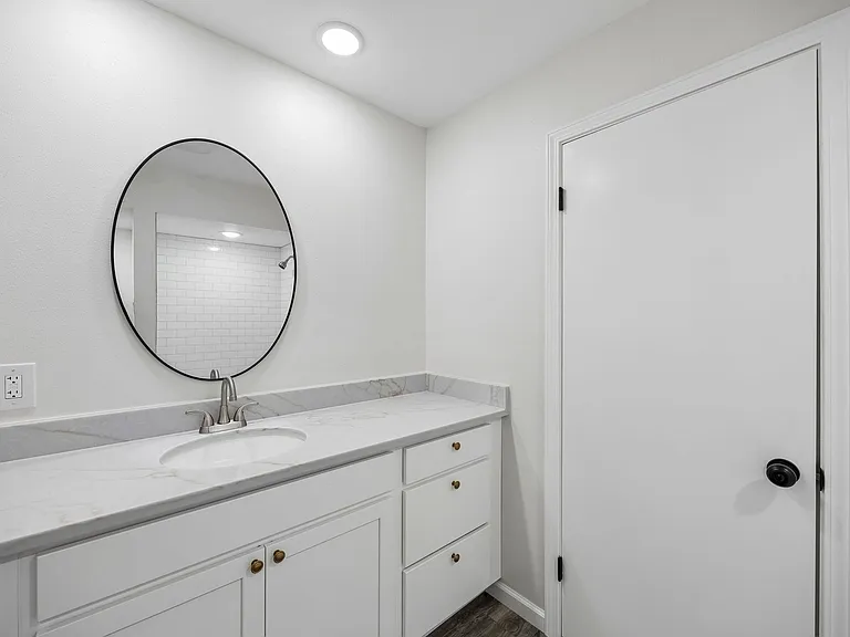 Modern vanity featuring white cabinetry, a light-toned countertop, and a circular black-framed mirror