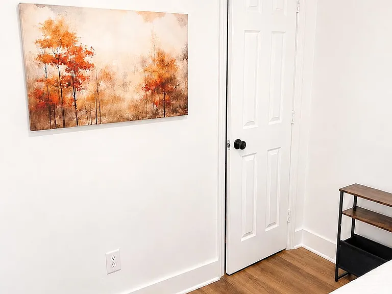 Clean bedroom corner with wood-look flooring, white walls, and a closet door, plus space for a small nightstand.