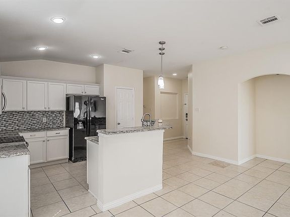 Kitchen featuring hanging light fixtures, black refrigerator with ice dispenser, white cabinetry, backsplash, and an island with sink