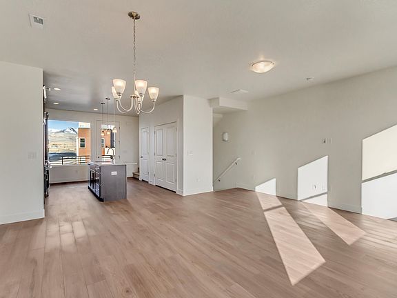 Spacious, unfurnished open-plan living area with wood flooring, kitchen island, and chandelier.