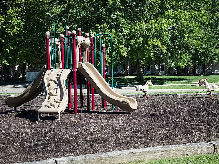 Inviting playground with modern slides and playful ride-on toys set in a lush green park area.