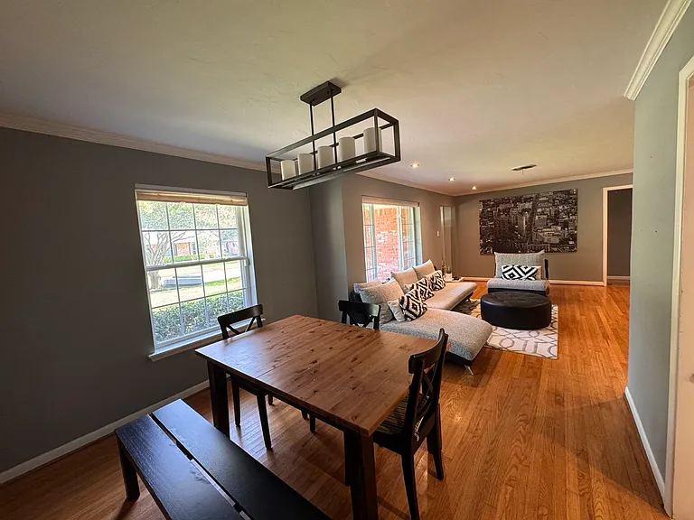 Dedicated dining area illuminated by a striking, modern linear chandelier and flanked by a large window looking out onto the front lawn, an ideal setting for family dinners or hosting guests.