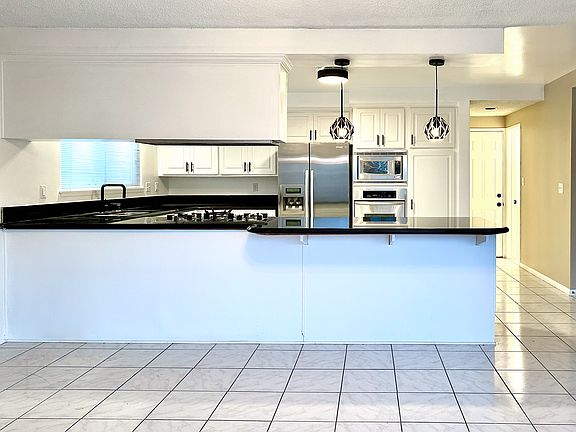 Large kitchen with gas cooktop, stainless steel appliances (fridge with water filter and ice maker), microwave, oven, dishwasher, large peninsula with overhang counter seating, opens to dining room and slider door leading to backyard.