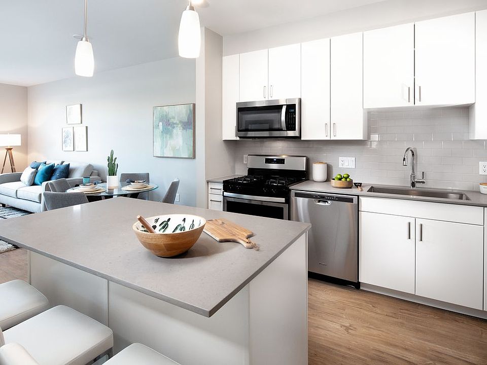 Modern kitchen with white cabinetry, tile backsplash, grey quartz countertops, stainless steel appliances, and hard surface flooring (Representative photo)