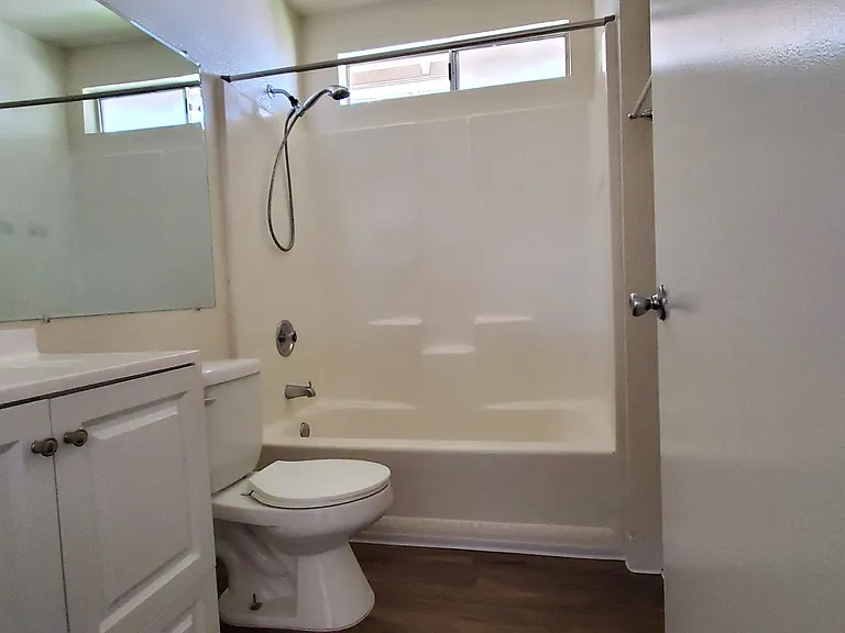 White bathroom with hardwood floor and natural light at Zenith Place Apartments in Chula Vista, California.