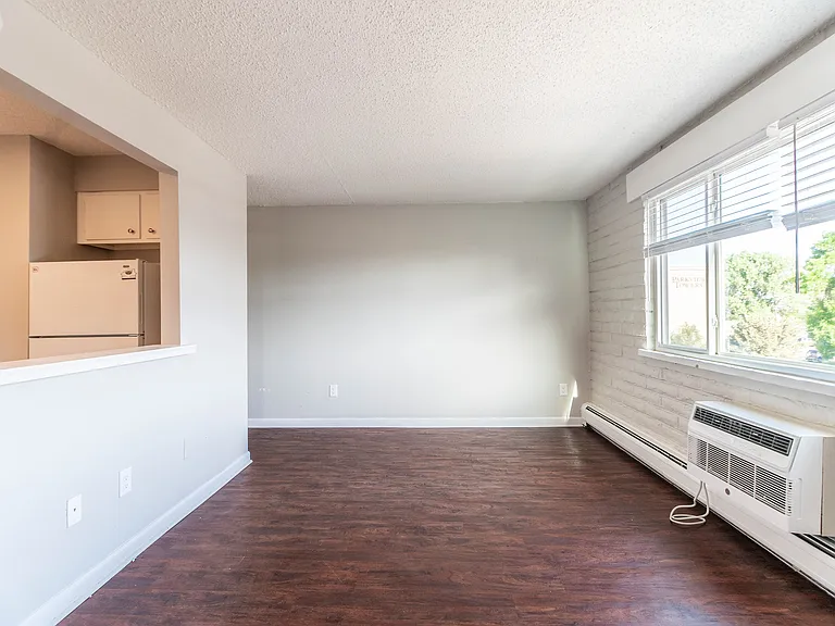 Bright living area with elegant wood flooring and large window offering garden views, adjacent to a cozy kitchen space.
