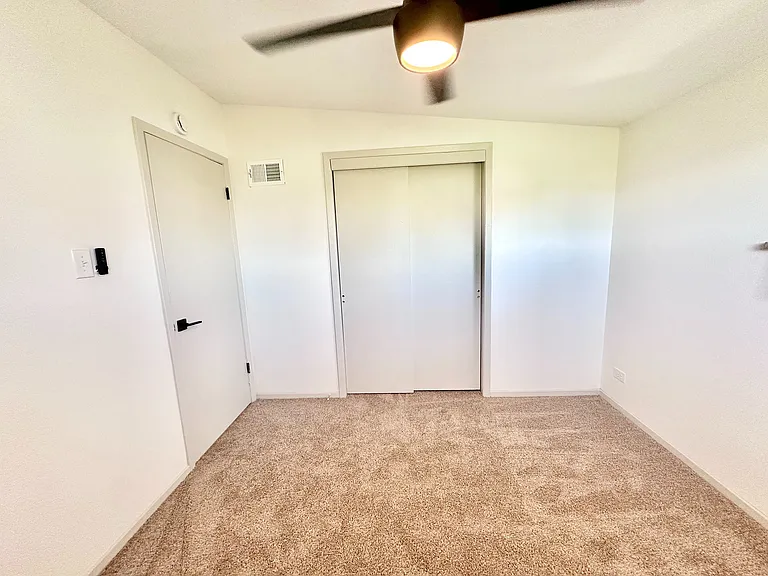 Bright, carpeted room with modern ceiling fan and sleek closet doors, perfect for customization and comfort.