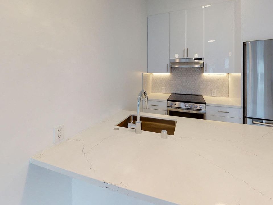 Kitchen with multiple cabinets, refrigerator, stove, range hood, and sink