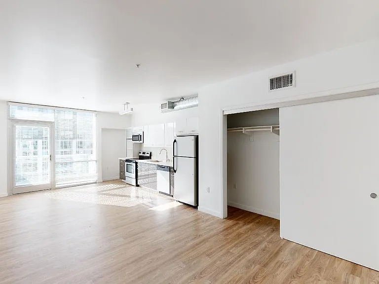 Apartment kitchen with stainless steel appliances, dining and living room with wood-style flooring.