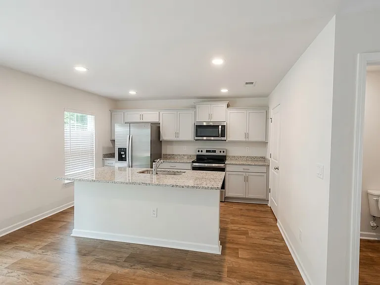 Complete kitchen featuring white shaker cabinetry, stainless-steel refrigerator, electric range, over-the-range microwave, and granite counters. The center island provides extra prep space and seating potential.