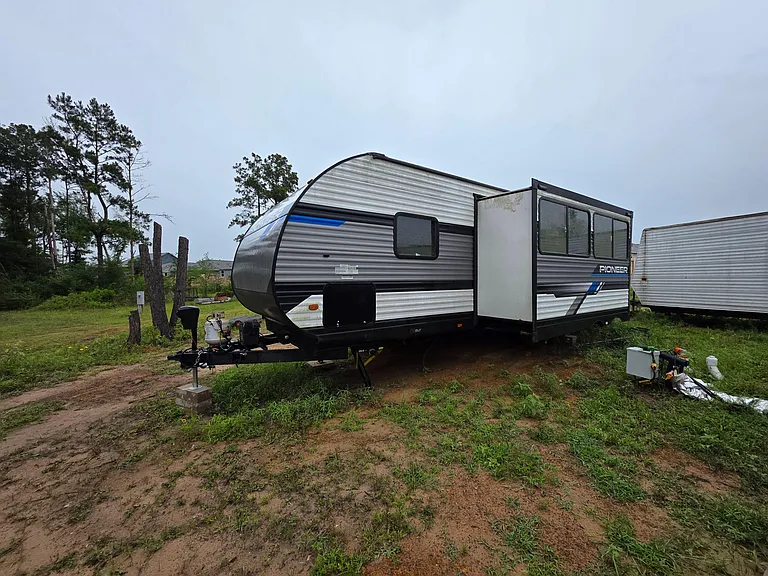 Private RV-style exterior set on a grassy lot with surrounding trees and convenient utility hookups nearby.