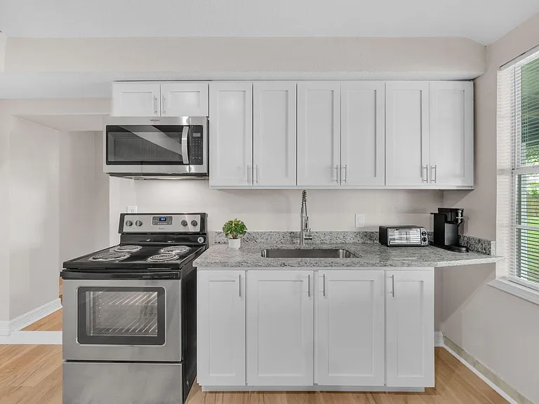 Efficient kitchen with ample white cabinetry, granite-look counters, stainless microwave, range, and a window-side sink.