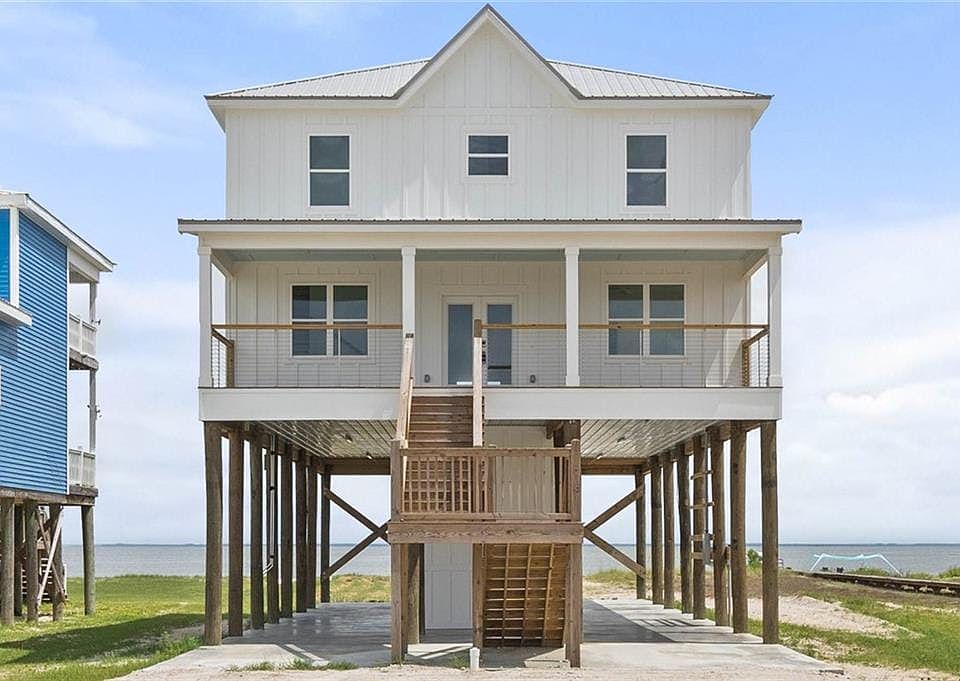 Raised beach house with board and batten siding, stairs, a water view, covered porch, and a metal roof