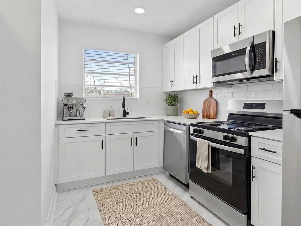 Modern white kitchen with stainless steel appliances and sleek cabinetry, illuminated by natural light.