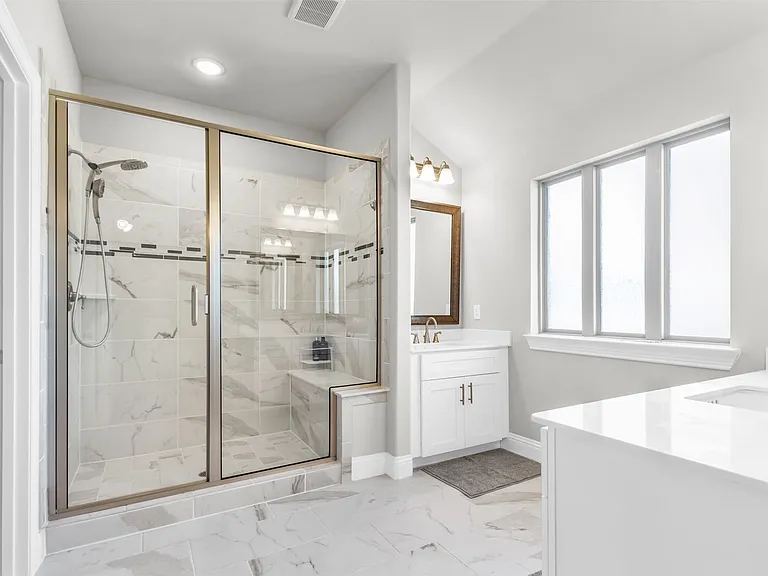 Spacious bathroom featuring a glass-enclosed shower with a built-in bench, marble-finish tile, and a dual shower head