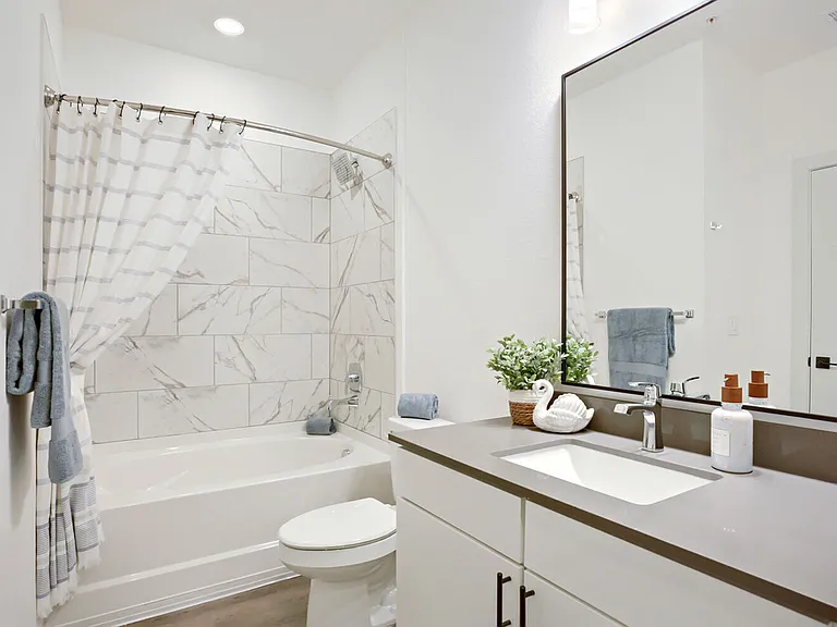 Marble-look tile surrounds and frameless mirrors elevate the everyday. Clean, modern bathrooms at Garrett Harvest Junction West, Longmont, CO.