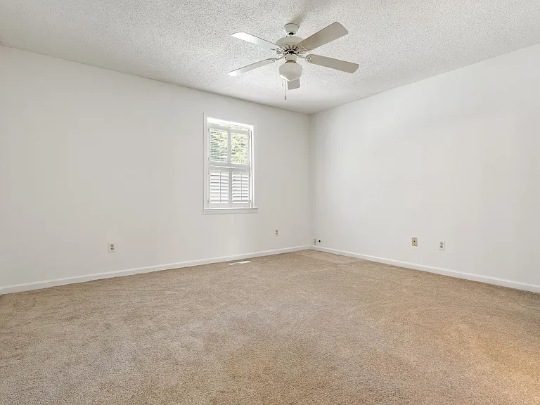 Generously sized primary bedroom with ceiling fan, plantation-shuttered window, and fresh neutral paint