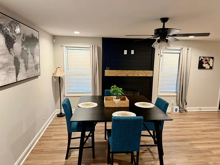 Dedicated dining area with a 4-seat table, two windows with curtains, and a ceiling fan for comfortable everyday meals.