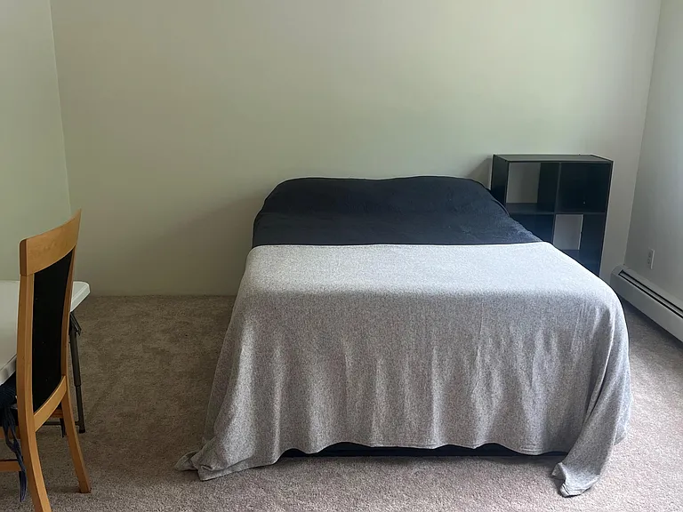 Carpeted bedroom with ceiling fan, baseboard heating, and space for a bed plus desk or storage shelving.