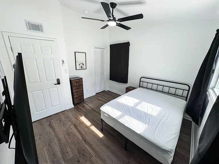 Private bedroom with wood-look flooring, ceiling fan, and a closet, furnished with a bed and dresser near a window.