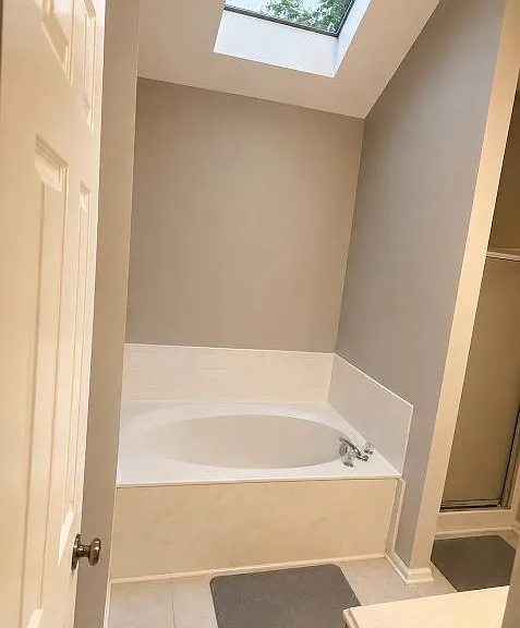 Spacious bathroom featuring a soaking tub with tile surround and a skylight that brings in natural light.