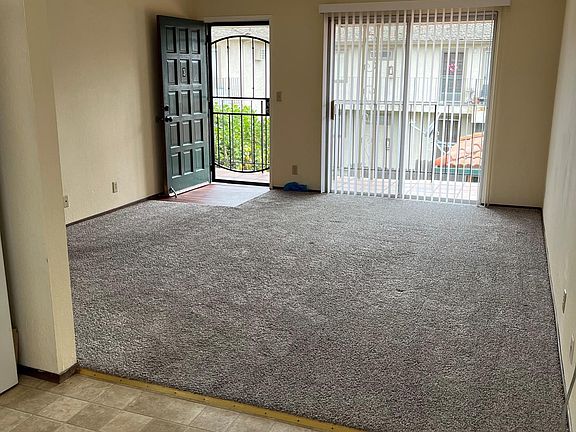 Photo of living room from kitchen dining area. Showing front door and sliding glass door/balcony with lemon tree.
