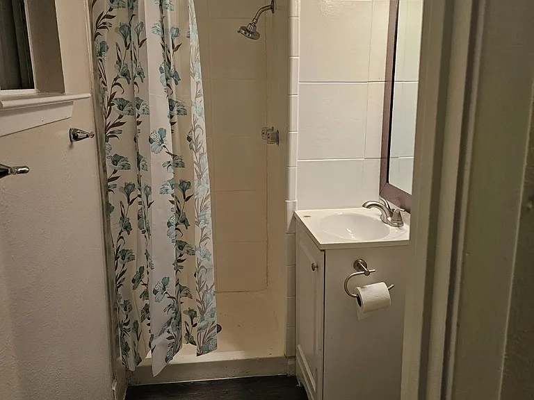 Compact full bath with shower combo, tiled surround, vanity with mirror lighting, and durable plank-style flooring.