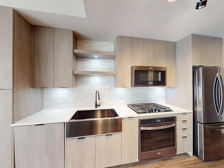 Apartment kitchen with stainless steel appliances, quartz countertops, and wood-style flooring.