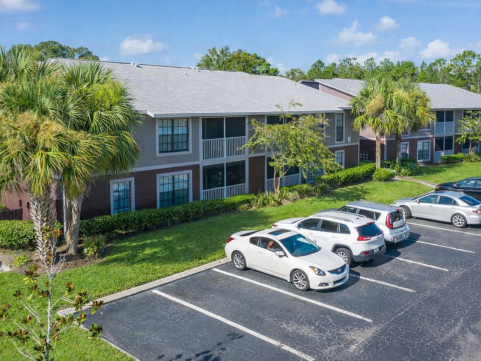 Charming two-story apartment complex surrounded by lush greenery and palm trees, featuring ample parking and modern design.