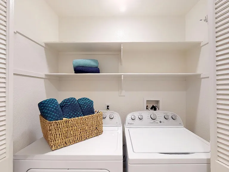 In-unit laundry closet with full-size washer and dryer, plus built-in shelving for supplies and linens.