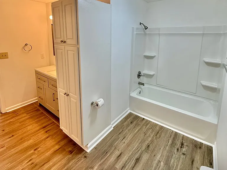 Bright modern bath retreat_ - grey shaker vanity with granite countertop and ample drawer space for organized storage - tub/shower combo and vinyl plank floors ensure a sleek, low-maintenance start to every day.