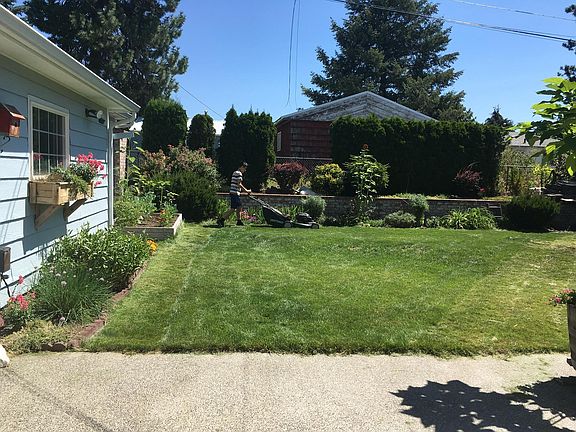 The side of the garage, looking from the back patio. The brick wall at the back of the yard is a retaining wall; the hedge and shrubs are planted above the wall.