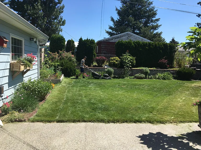 The side of the garage, looking from the back patio. The brick wall at the back of the yard is a retaining wall; the hedge and shrubs are planted above the wall.