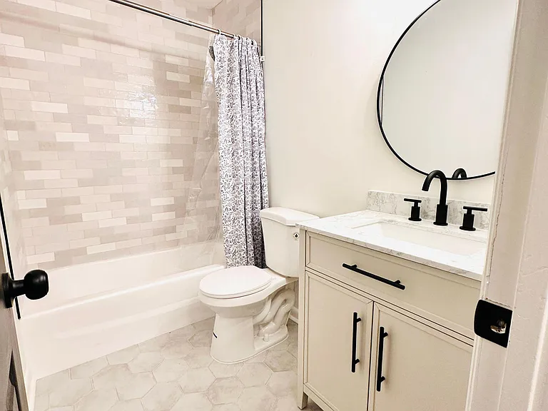 Updated full bath with tiled tub/shower, wide vanity storage, marble-look top, and modern matte-black fixtures.