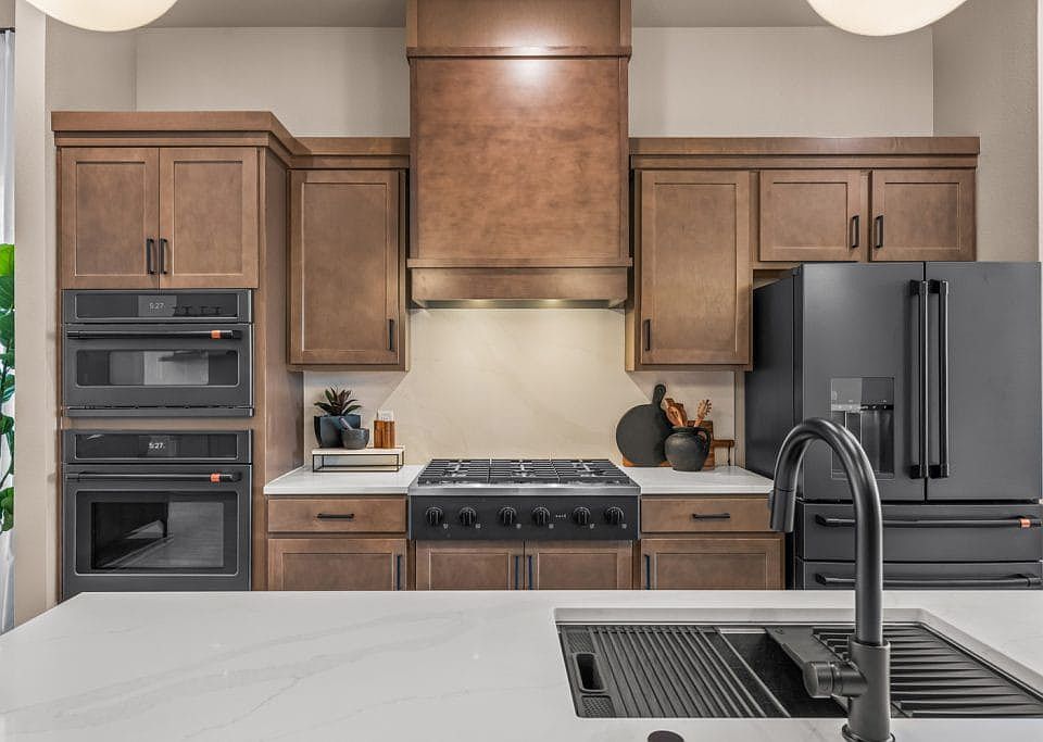 Modern kitchen with wood cabinets, a black refrigerator, double wall ovens, a gas stove, and a range