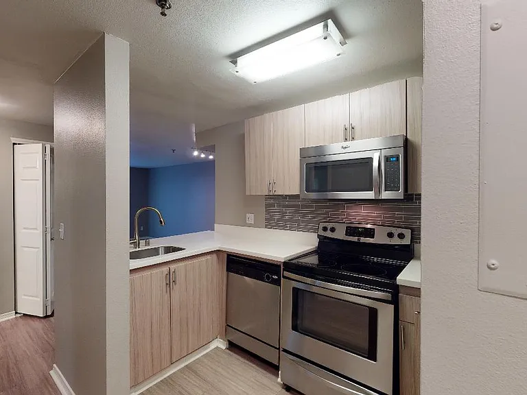 Apartment kitchen with stainless steel appliances, quartz countertops and wood-style flooring.