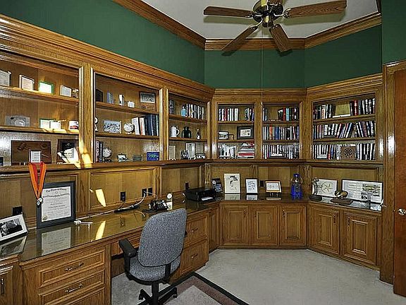 French door entrance with spacious work area, built in desk, rows & rows of bookshelves, storage closet & a ceiling fan.