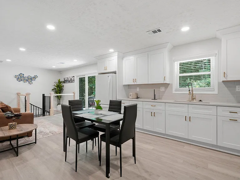 Open-concept kitchen with ample white cabinetry, long counters, and a dining area beside a large window and patio door.