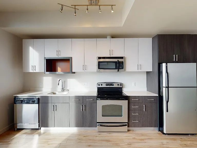 Apartment kitchen with stainless steel appliances, quartz countertops and wood-style flooring.