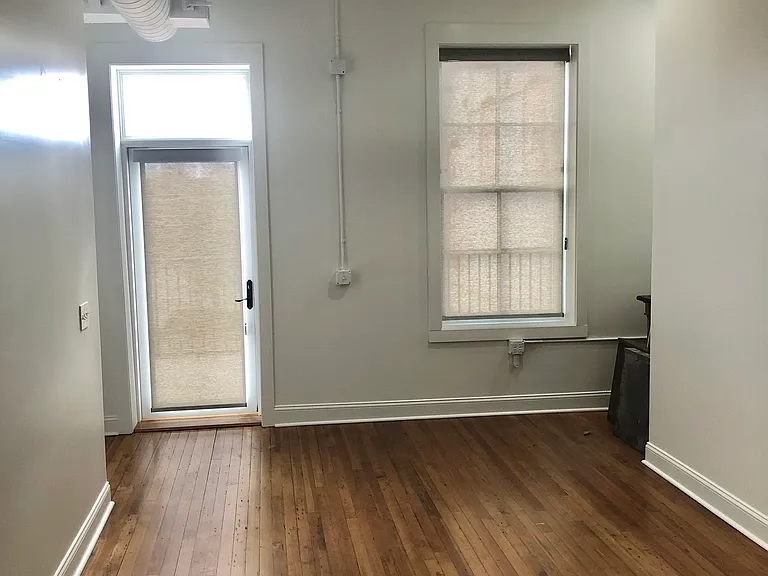 Doorway to large outside patio with open city view. Window for the living room. Both door and windows have custom shades.