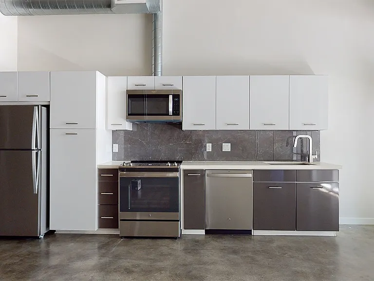 Apartment kitchen with stainless steel appliances, quartz countertops and polished concrete or wood-style flooring.
