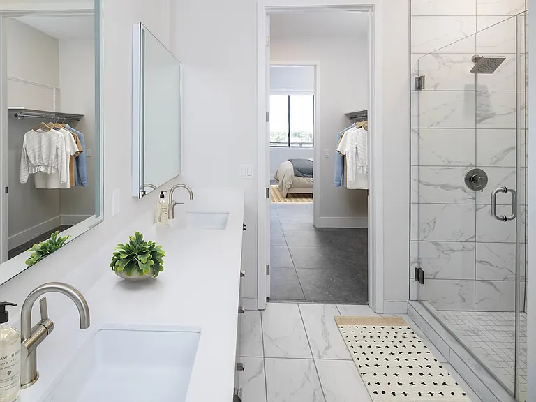 Signature Collection bathroom with grey cabinetry, white quartz countertop, lighted vanity mirrors, porcelain shower surround, and porcelain tile flooring
