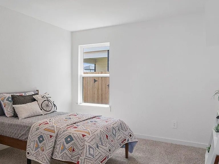 Neat bedroom with a comfortable bed layout, carpeted floors, and a window for natural light and ventilation.