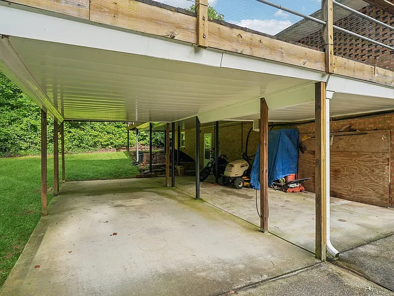 A covered lower level patio tucked beneath the deck, offering generous outdoor storage, shaded workspace, and a practical extension of the home with woodland charm.