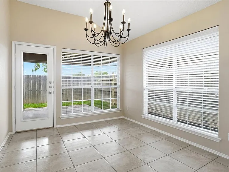 Dining area featuring a vaulted ceiling with an overhead chandelier, large windows with blinds, a glass-paneled door, and square tile flooring